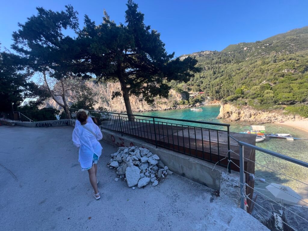 Woman walking beside a railing overlooking a Paleokastritsa bay and wooded hills