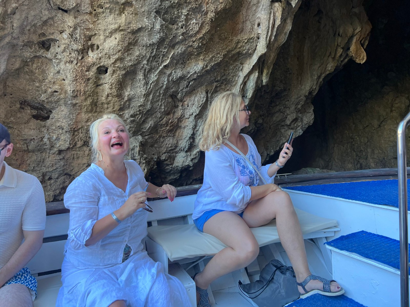 Two women on the boat beside a sea cave wall
