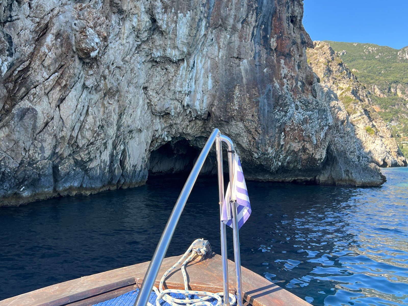 View over the boat bow towards a low cave opening beneath pale cliffs