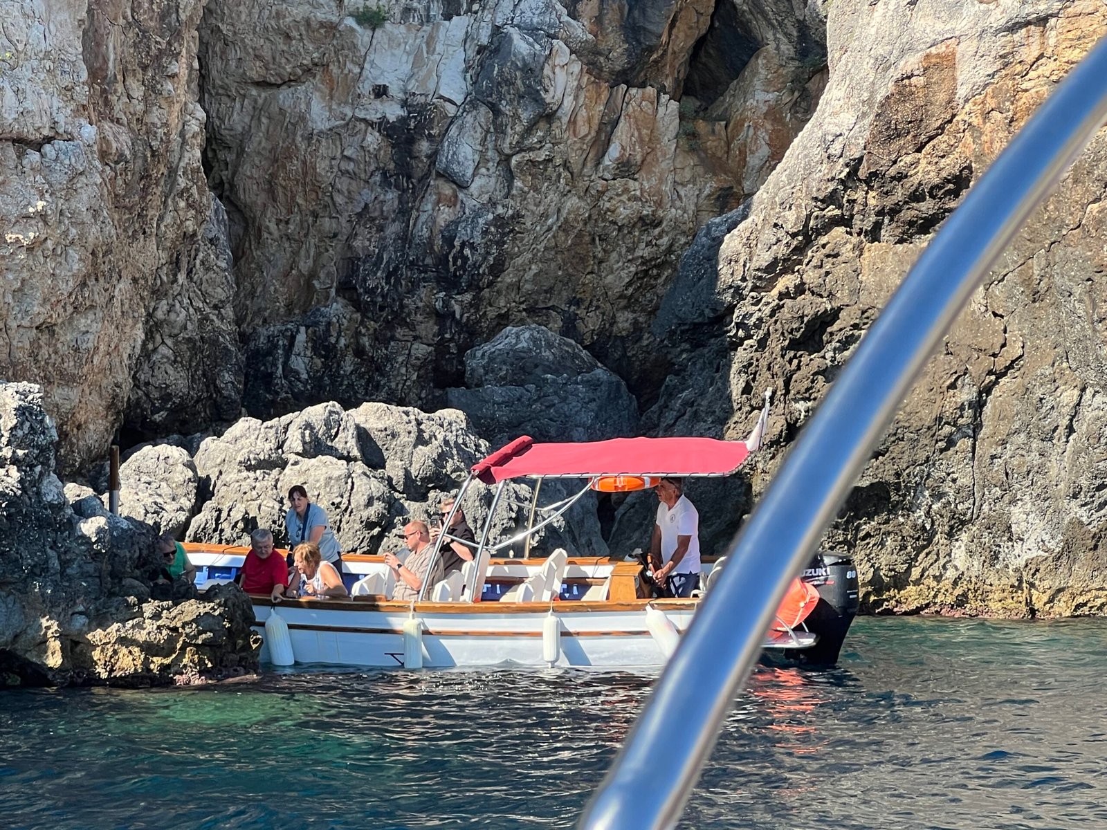 Another small sightseeing boat with a red canopy beside the cliffs