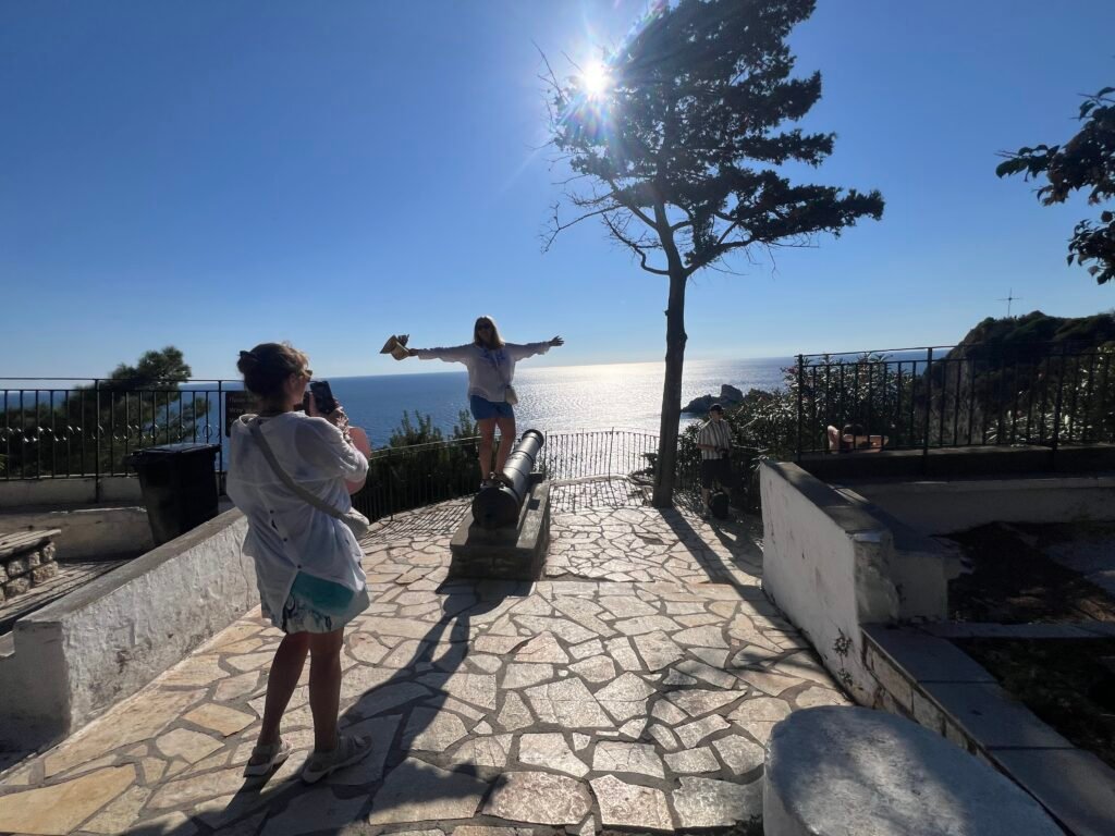 Visitors photographing the Ionian Sea from a stone terrace near Paleokastritsa Monastery